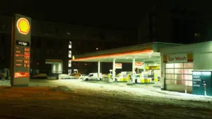 Degvielas uzpildes stacija naktī ar redzamu cenu tablo un sniegu uz zemes.