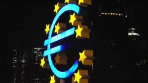 Spilgts izgaismots eiro simbola monuments pilsētas naktī, simbolizējot Eiropas Centrālās bankas politiku.