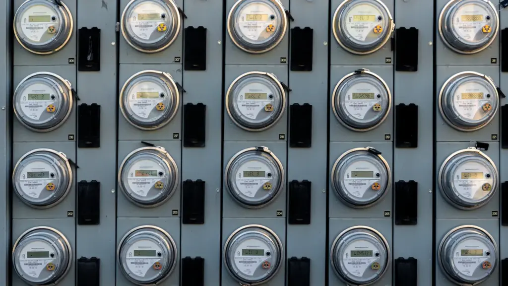 Melnbalts elektrības skaitītājs pie sienas, kas simbolizē pieaugošās energoresursu izmaksas Latvijas mājsaimniecībās.