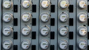 Melnbalts elektrības skaitītājs pie sienas, kas simbolizē pieaugošās energoresursu izmaksas Latvijas mājsaimniecībās.