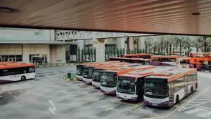Rindā stāvoši sabiedriskā transporta autobusi stacijas teritorijā pirms došanās reisos.