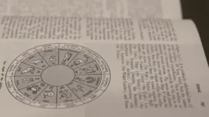 Atvērta grāmata ar detalizētu zodiaka zīmju apli un paskaidrojošu tekstu.