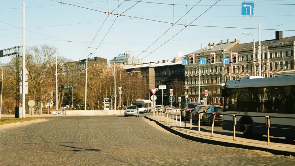 Iela Rīgā ar sabiedrisko transportu un automašīnām, kas atspoguļo pilsētas satiksmes ikdienu.