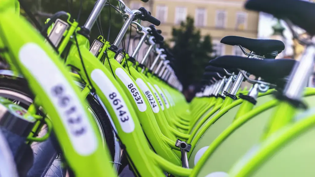 Rinda ar koši zaļiem īres velosipēdiem pilsētas ielas malā pirms mobilitātes nedēļas