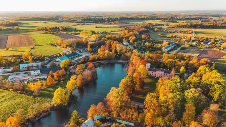 Latvijas mazpilsēta un upe rudens krāsās no putna lidojuma skatpunkta.