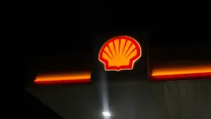 Degvielas uzpildes stacijas logotips naktī, simbolizējot degvielas cenu izmaiņas un ekonomiskus lēmumus.